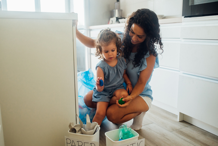 Happy young woman teaching her daughter to recycle