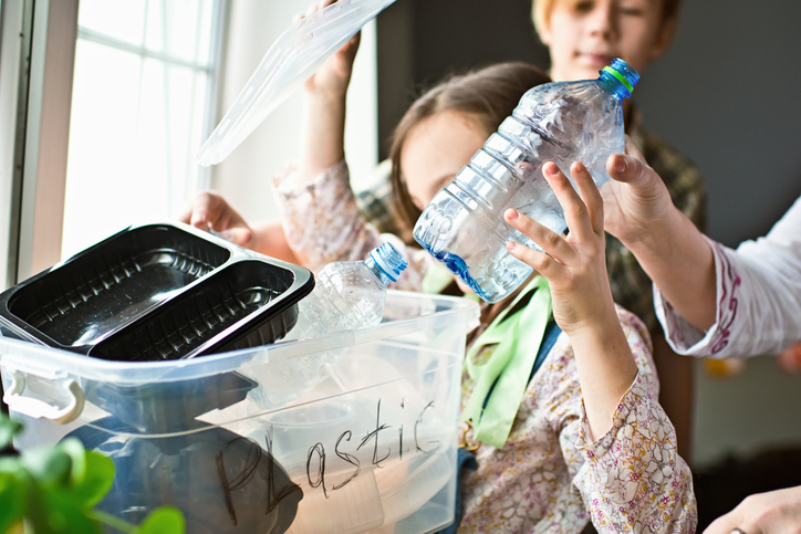 Mother teaching her children how to separate plastic, glass and paper waste at home