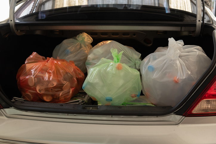 A car trunk filled with color-coded plastic bags containing recyclable materials such as bottles and containers.